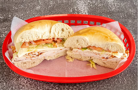 A sliced sandwich with turkey, cheese, lettuce, and tomato is in a red plastic basket lined with wax paper on a textured surface.