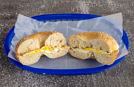 A sesame bagel with egg and cheese, cut in half and placed on wax paper in a blue plastic basket.