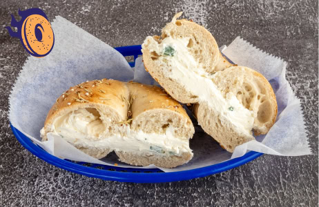A sliced bagel with cream cheese filling is placed in a blue plastic basket lined with white paper on a textured surface.