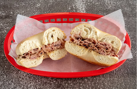 A sliced bagel filled with thinly sliced roast beef sits on wax paper in a red plastic basket on a gray surface.