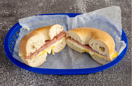 A bagel sandwich with egg, cheese, and meat is cut in half and served on wax paper in a blue plastic basket.