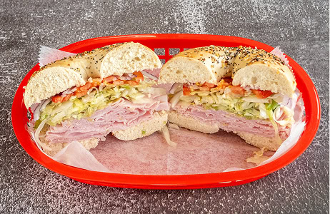 A bagel sandwich with turkey, shredded lettuce, and tomato slices in a red basket on a textured gray surface.
